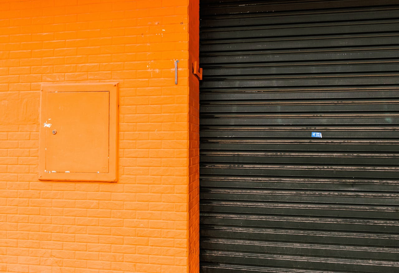 An orange-painted wall with imitation brick texture and a contrasting black roller door in an urban setting.